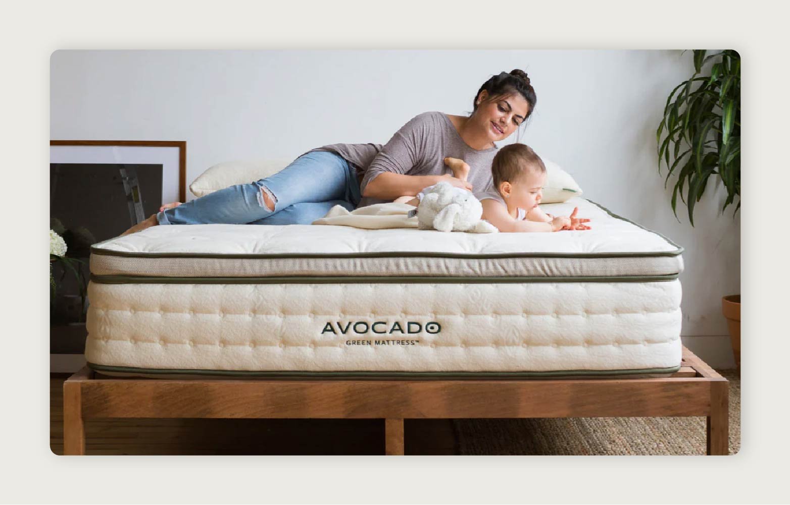 A woman and her baby lying on top of an Avocado Green Mattress with a painting and plant behind them.